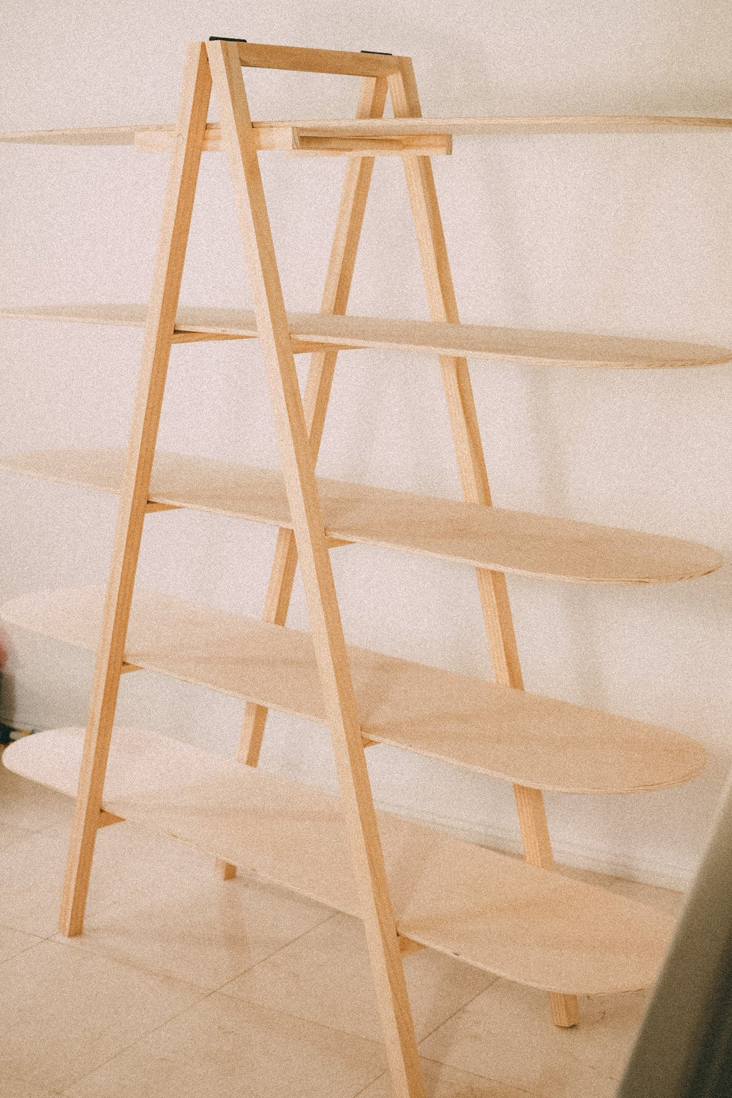 Empty wooden A-frame display viewed at an angle, showing five shelves with rounded ends and exposed timber supports.