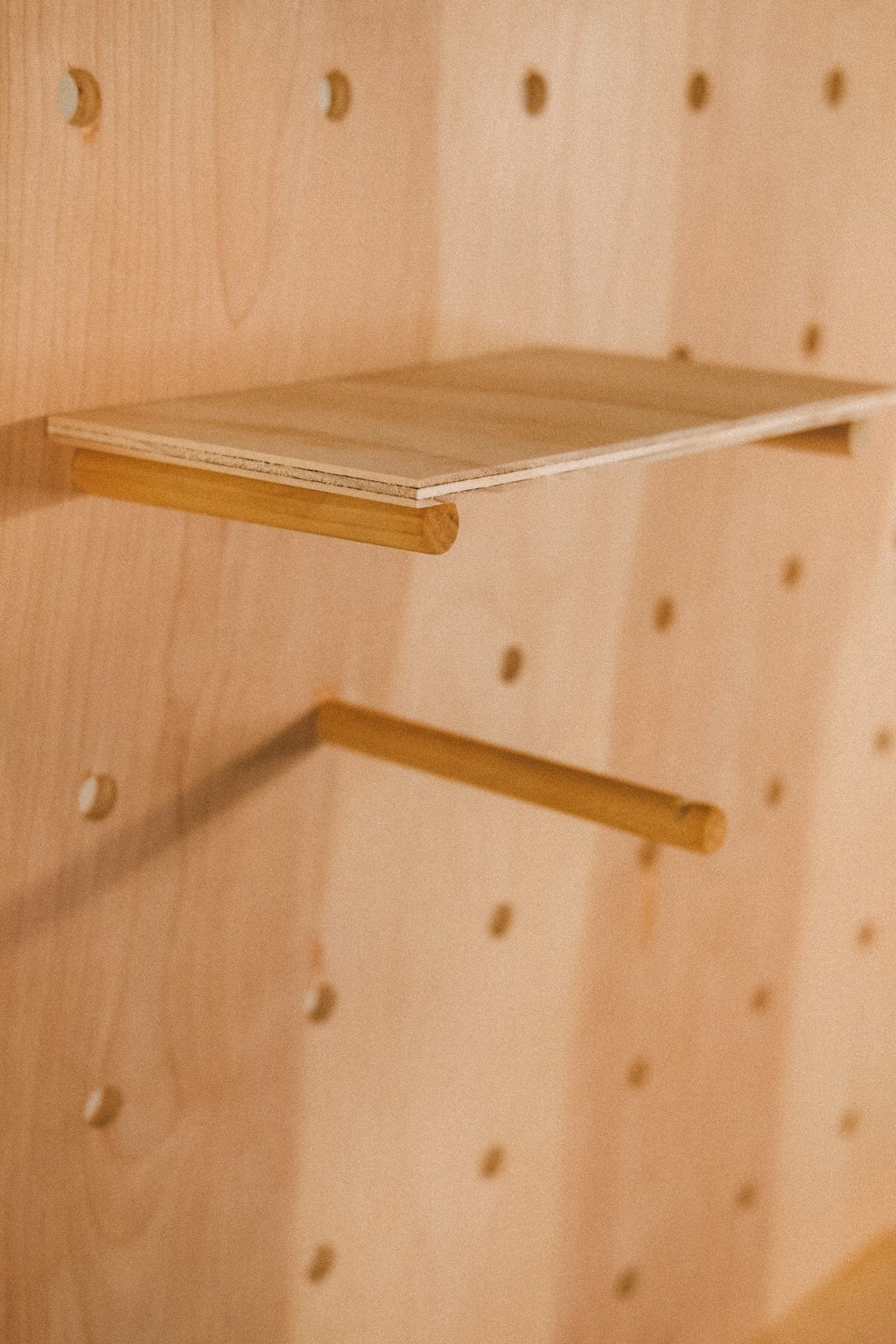 Close-up of a wooden pegboard shelf and a separate projecting peg against the regularly spaced round holes.