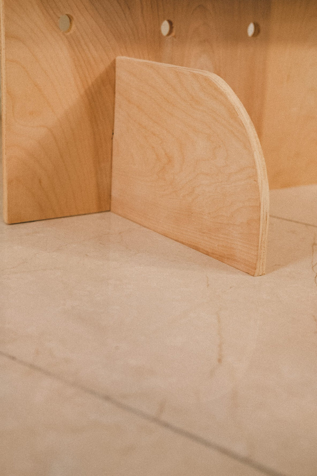 Close-up of a curved plywood foot supporting the freestanding pegboard on the floor.