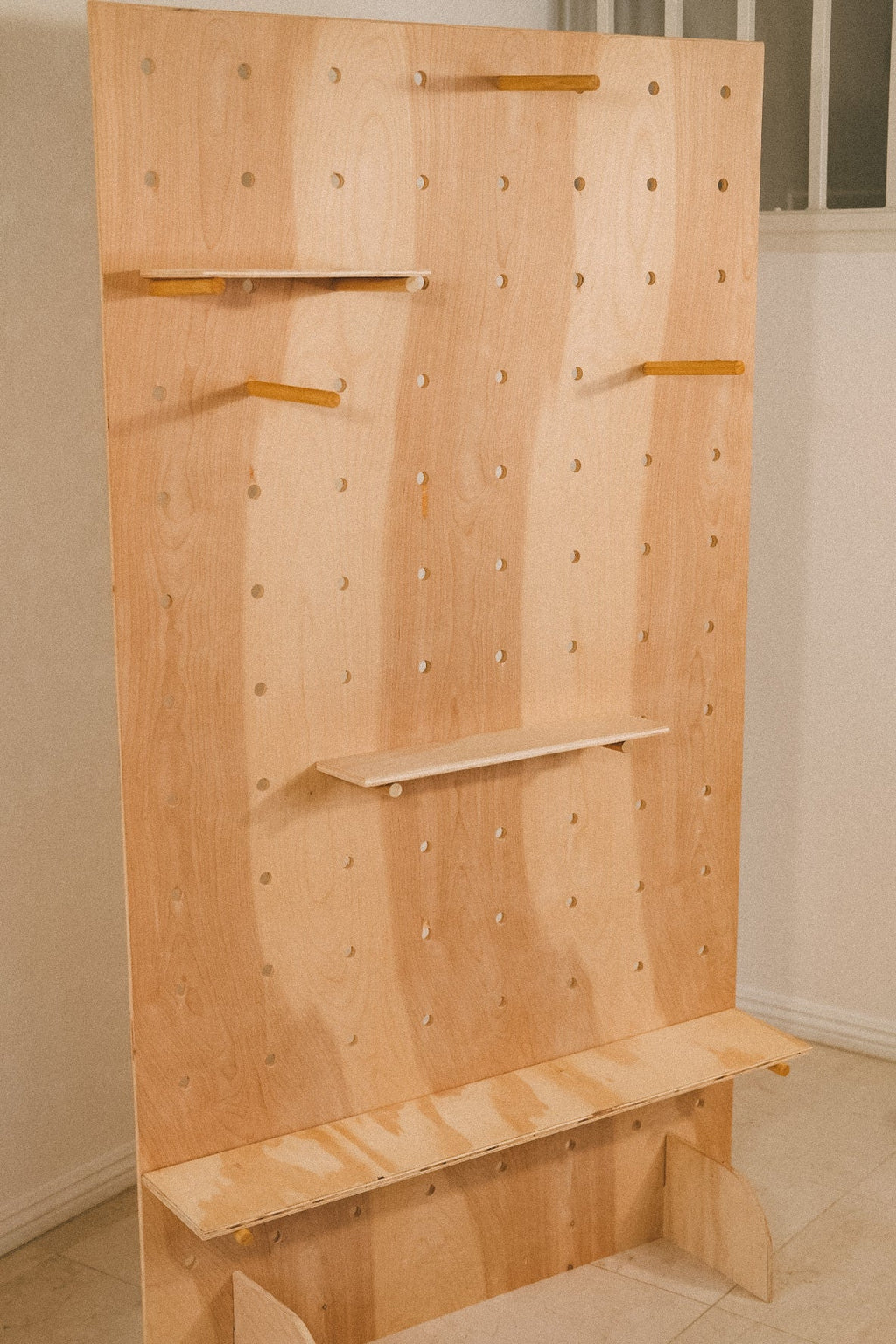 Angled detail of the empty wooden pegboard, showing the hole grid, projecting pegs and shelves at different heights.
