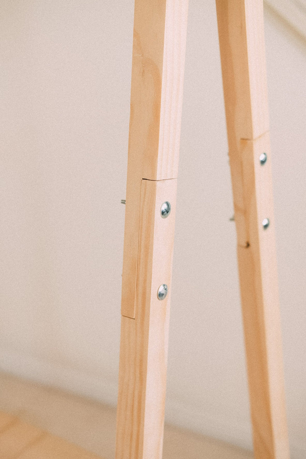 Close-up of the clothing rack's timber legs, showing the joins and exposed metal fasteners.