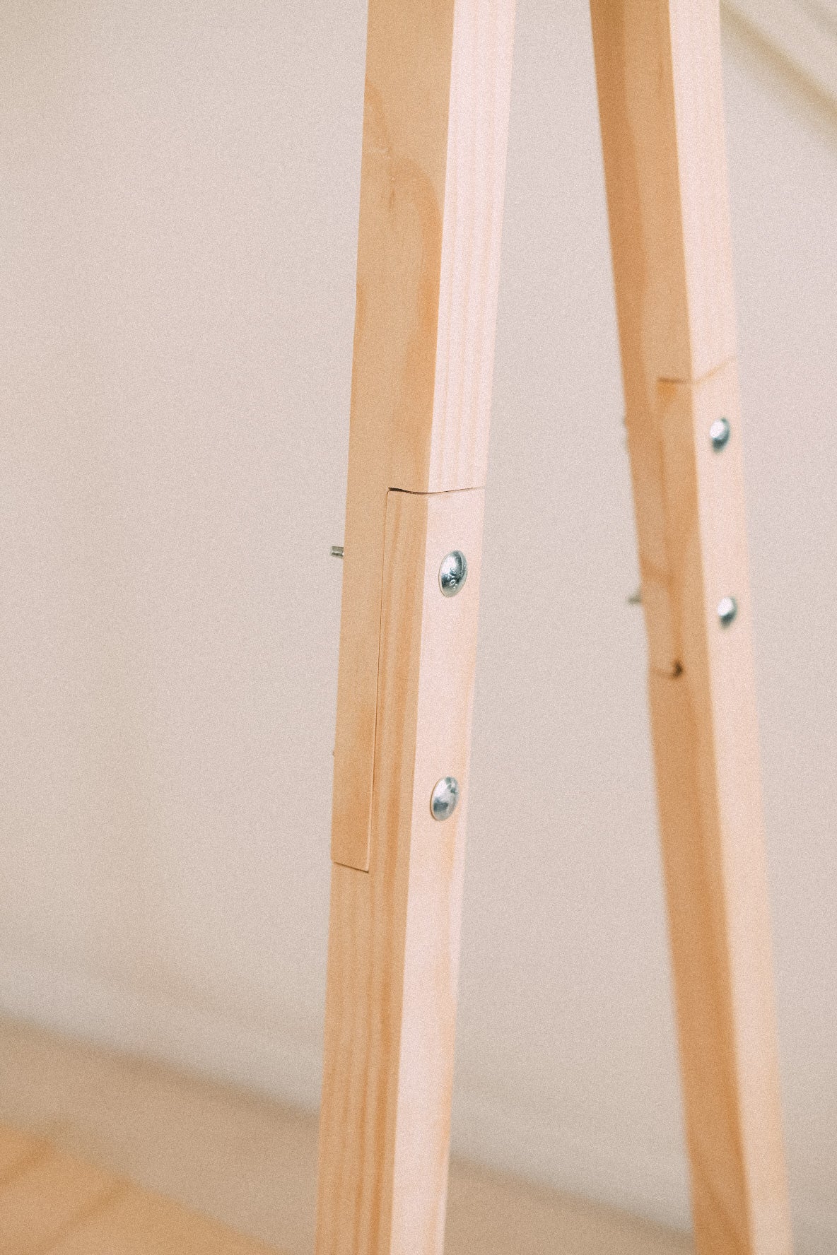 Close-up of the clothing rack's timber legs, showing the joins and exposed metal fasteners.