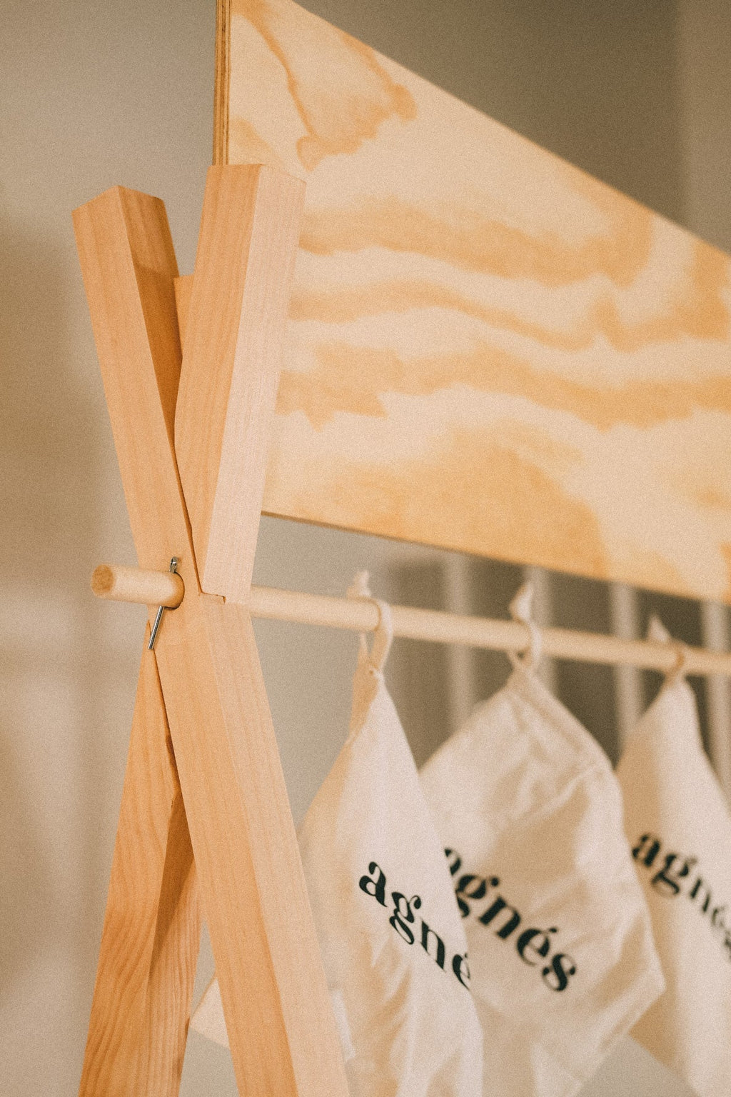 Close-up of a wooden display's upper frame joint and blank header board, with branded white bags hanging below.