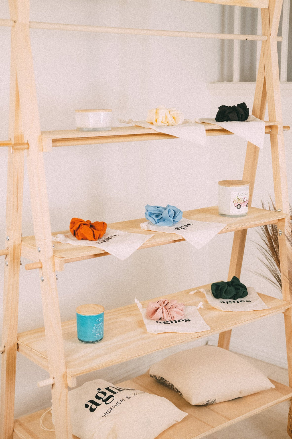 Detail of wooden market shelves with colorful scrunchies and small containers, with fabric bags on the bottom shelf.