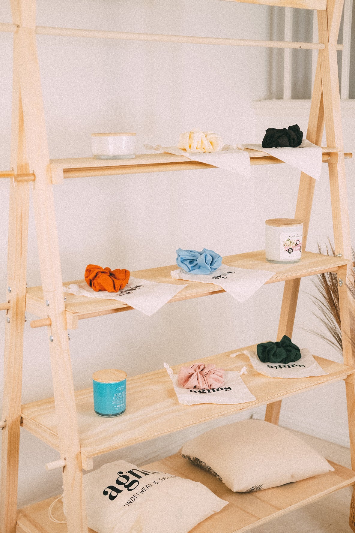 Detail of wooden market shelves with colorful scrunchies and small containers, with fabric bags on the bottom shelf.