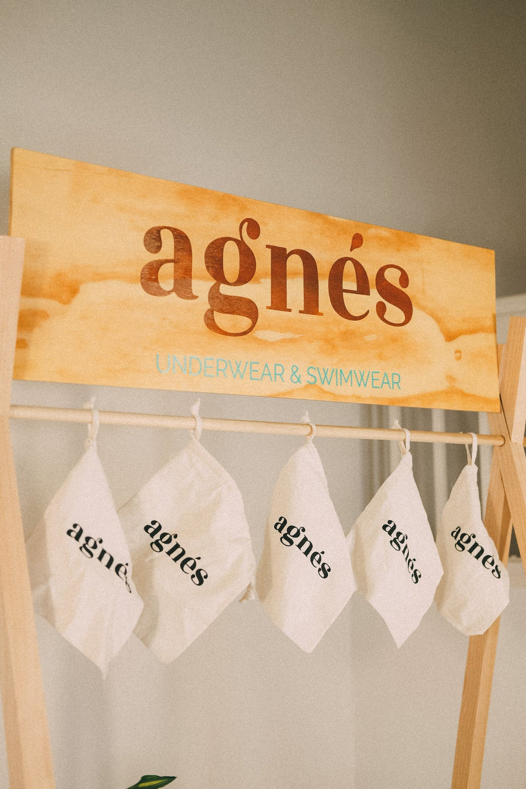 Wooden display header with an agnès logo above a rail of hanging white branded bags.