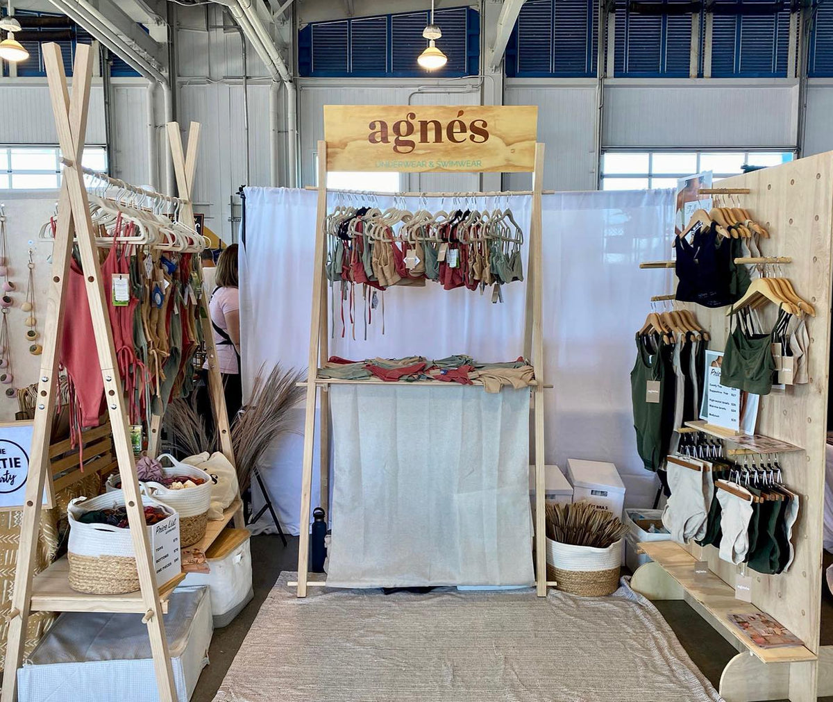 Indoor market booth with wooden clothing displays, a pegboard and an agnès counter stocked with swimwear.