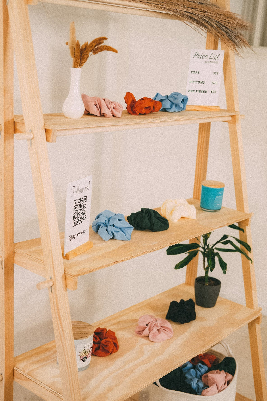 Close-up of wooden retail shelves with colorful scrunchies, a small potted plant and customer information signs.