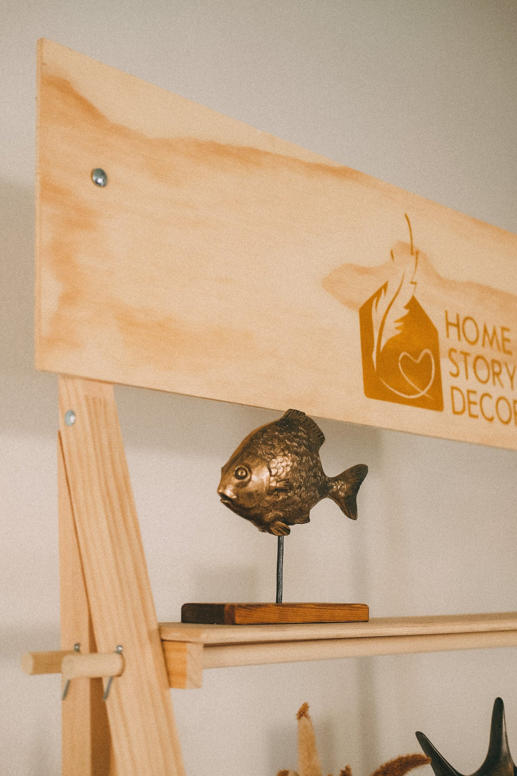 Close-up of a Home Story Decor header board above a decorative fish on a wooden display shelf.